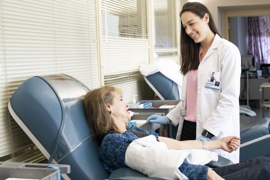 A clinician smiles and talks with a patient reclining in a medical chair during a clinical visit