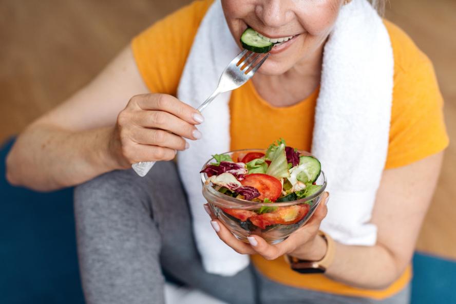 Senior woman wearing workout clothing, eating salad