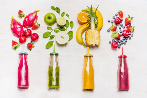 four glass bottles colored pink green yellow and purple with fruits and veggies coming out the top
