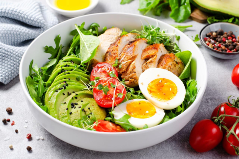 A bowl of salad with grilled chicken, hard-boiled eggs, and sliced avocado.