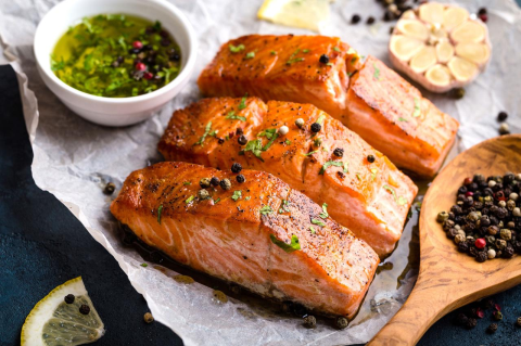 Three salmon fillets, cooked and resting on a dark countertop next to a wooden spoon and a 