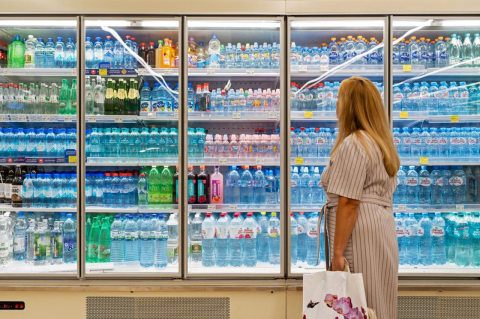 A woman stands in front of a cooler full of bottled water varieties.